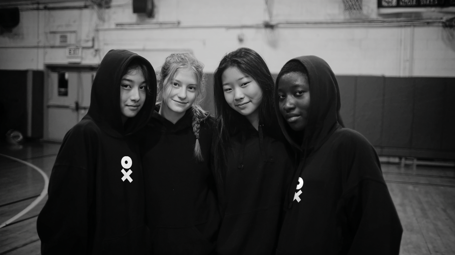 Four individuals wearing black hoodies with a logo in an indoor setting